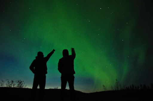 People pointing and watching northern lights overhead in Iceland