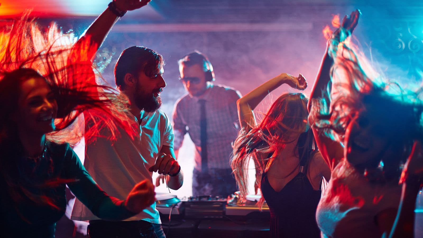 Group of people dancing at a club with a DJ in the background.