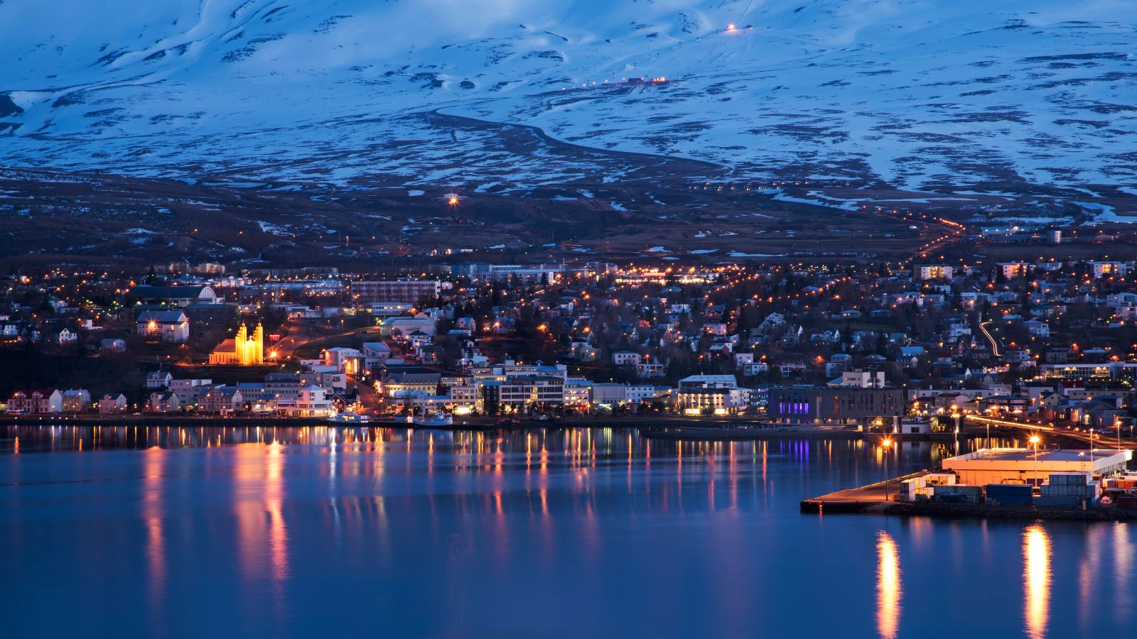 A late evening view of Akureyri across the fjord water overlooking the church, shopping streets, industrial docks, and private houses.