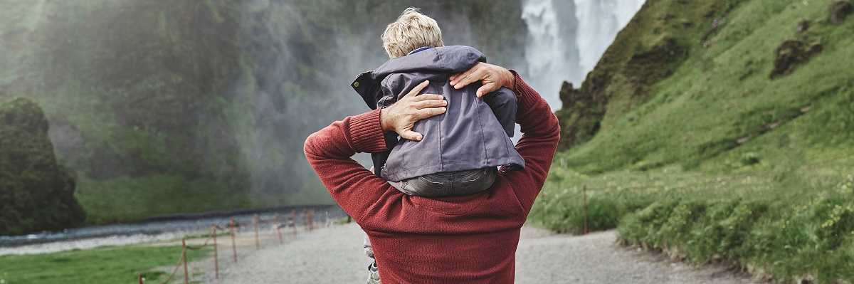 Son on father's shoulder near waterfall in Iceland