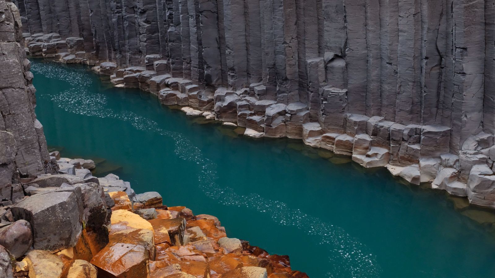 Bright blue waters and canyon walls of Stuðlagil Canyon in Iceland.