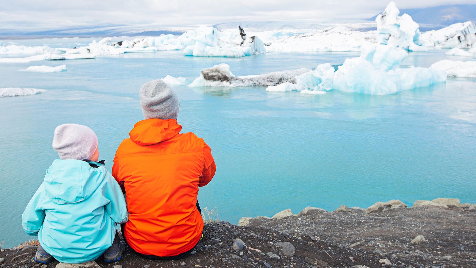 Child and parent sitting in front of a glacial lagoon in Iceland.