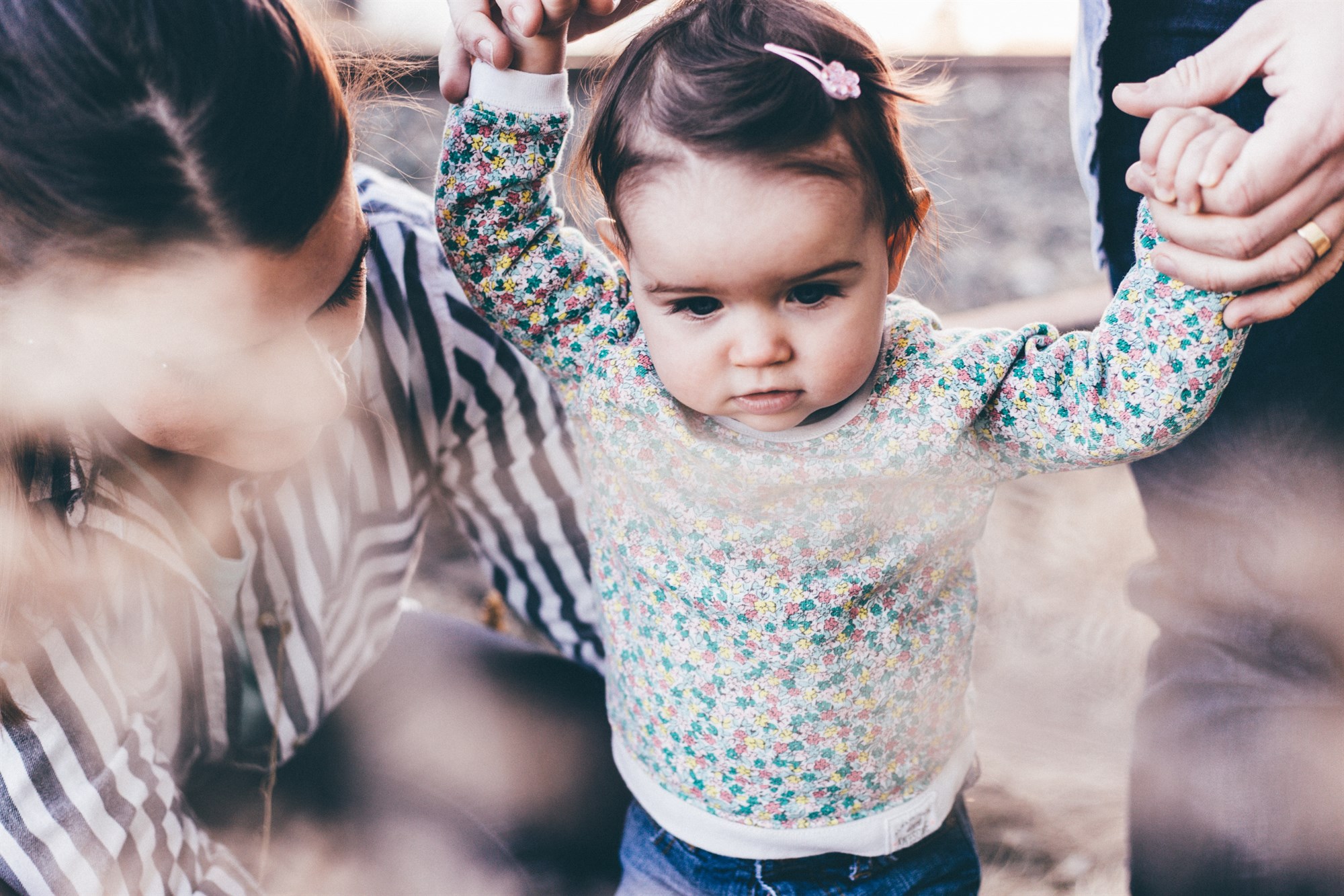 Parents holding a toddlers hands as she walks over rocks.