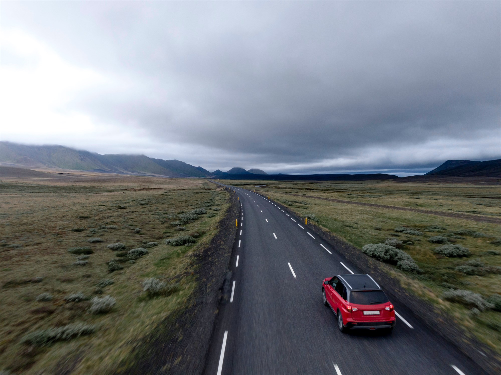  Red car driving on Icelandic road surrounded by flat landscape.