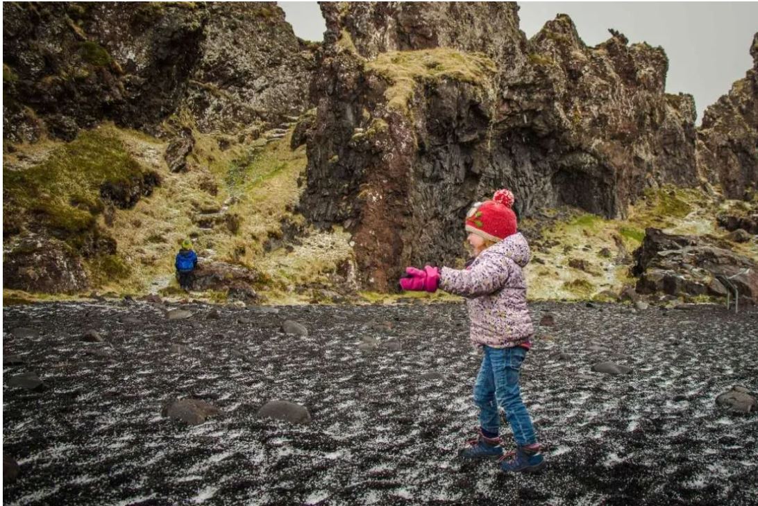 Little girl running along black sand beach in Iceland
