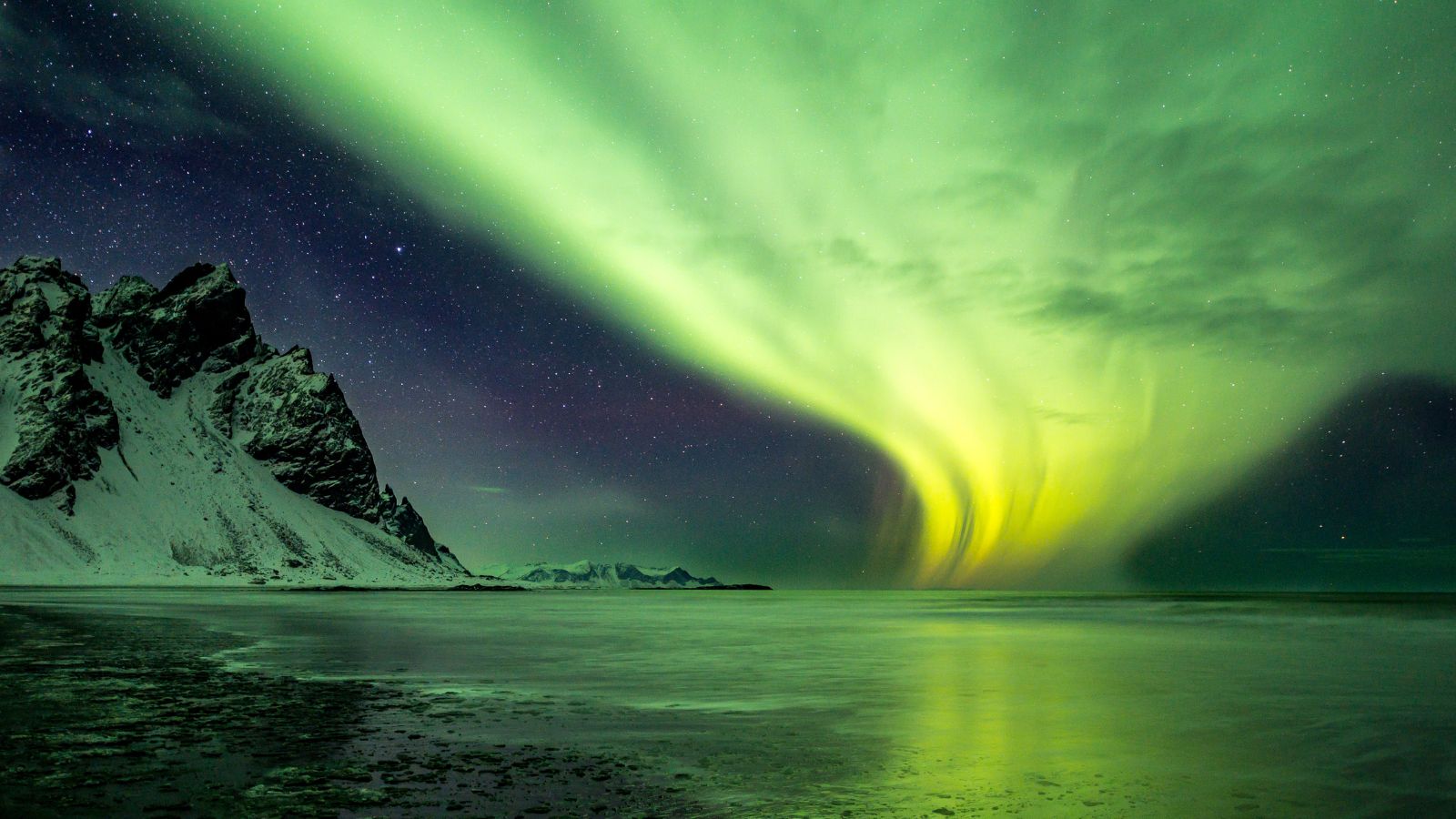 Bright green Northern Lights in a starry sky beside a mountain in Iceland.