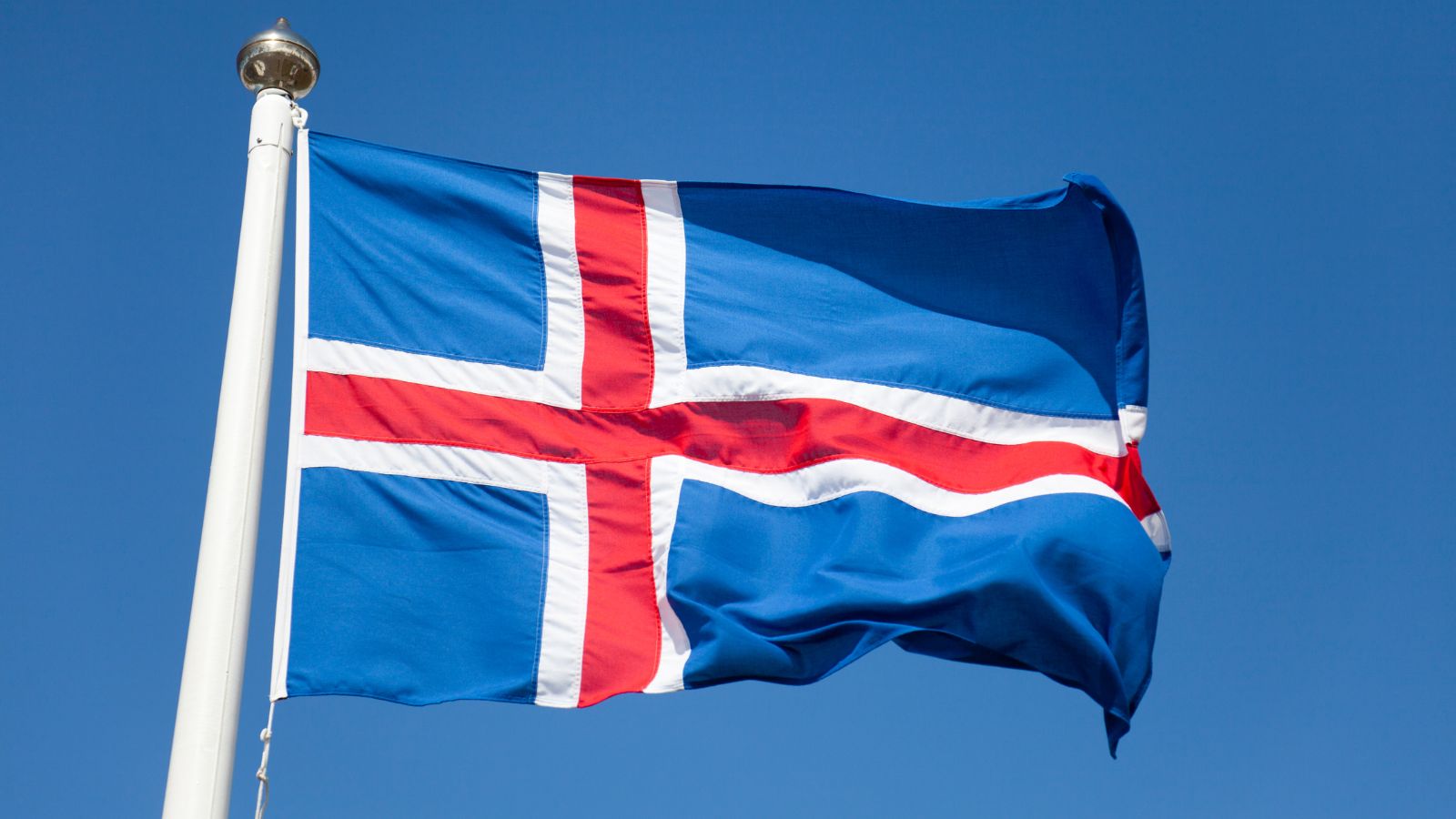 Icelandic flag on a white flag pole against the blue sky