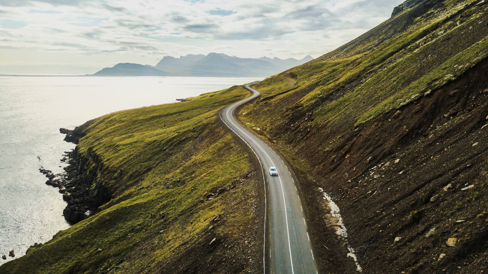 Winding road between a mountain and a body of water in Iceland.