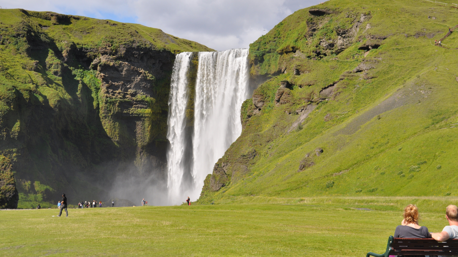A couple sitting on a bench watching a waterfall in Iceland.