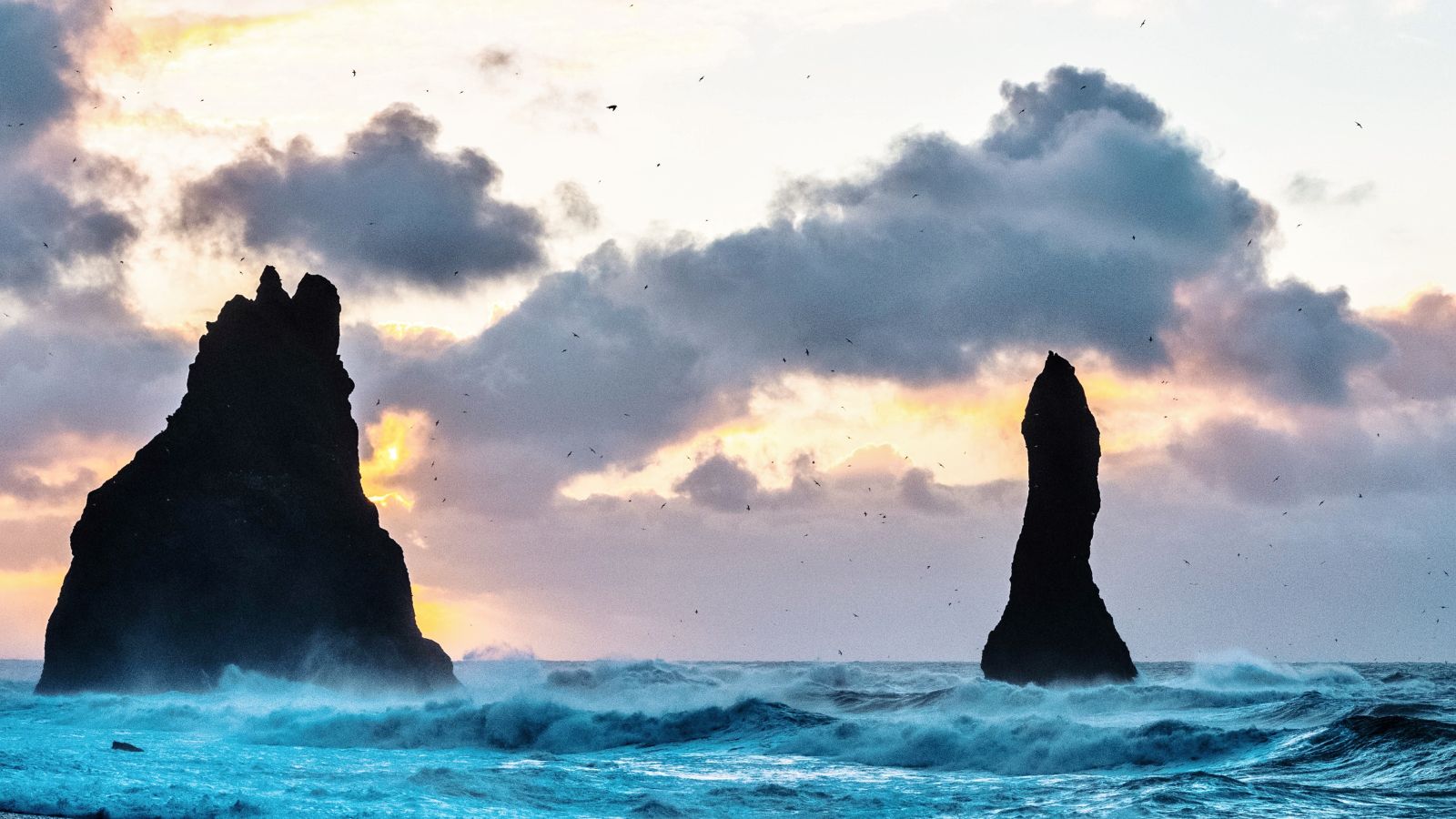 Sea stacks in the surf at sunset at Reynisfjara beach.