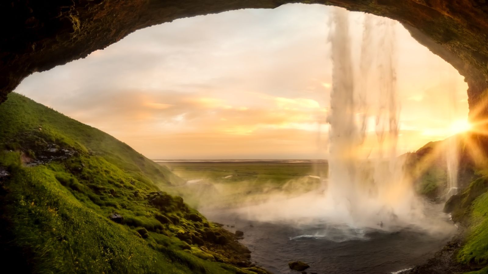 The view from behind Seljalandsfoss waterfall in Iceland at sunset.