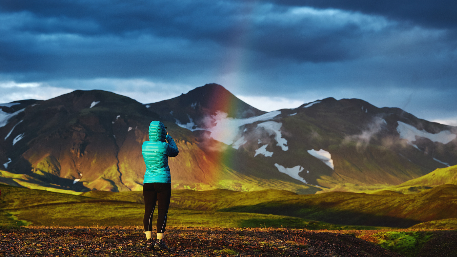 Hiker taking a picture of a rainbow while hiking in Iceland.