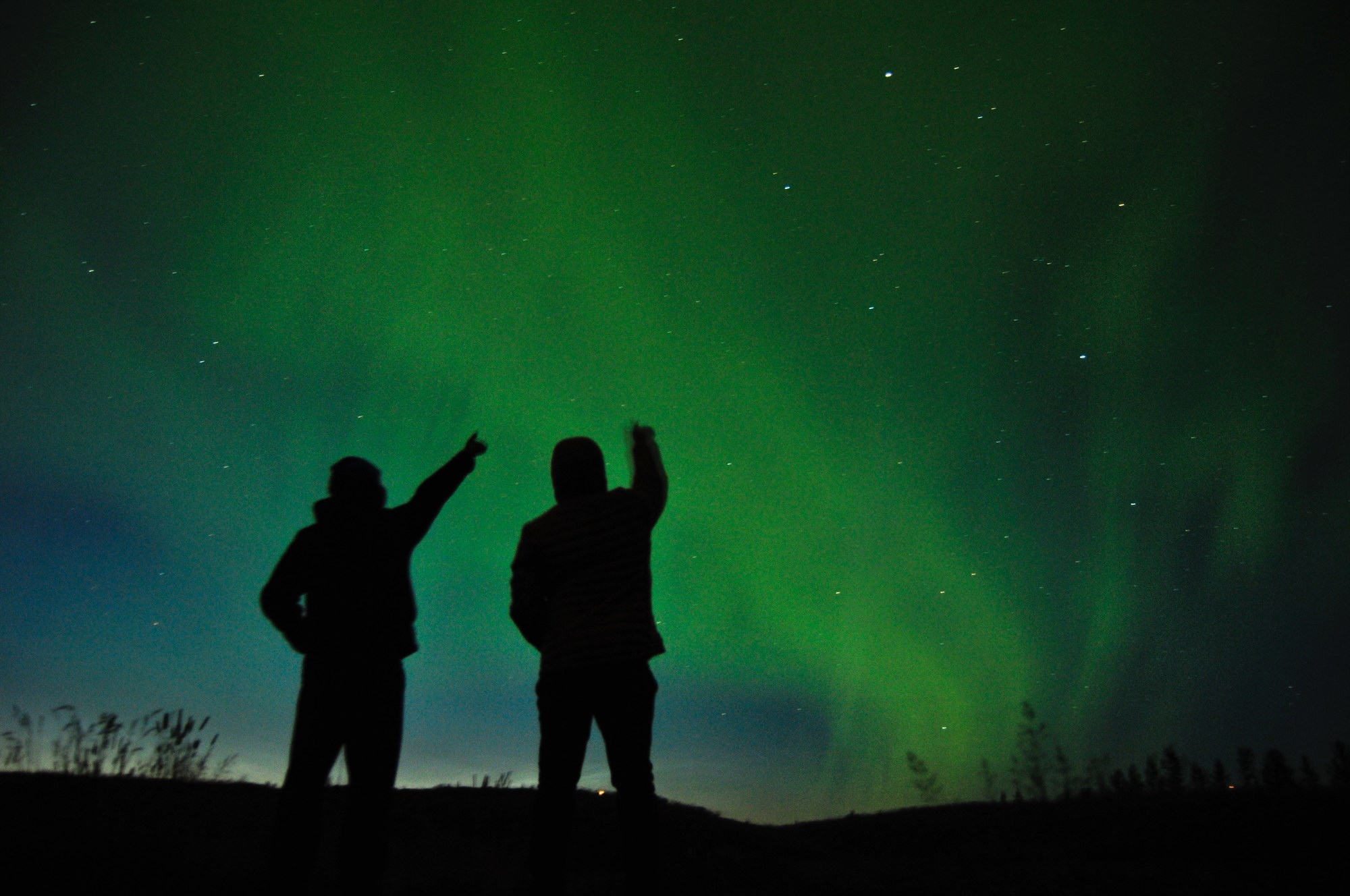 People pointing at the northern lights in a clear sky in Iceland